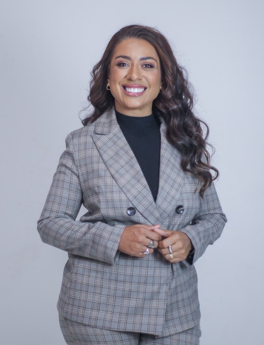 Priscila Lima sorrindo, de terno xadrez, em foto de estúdio